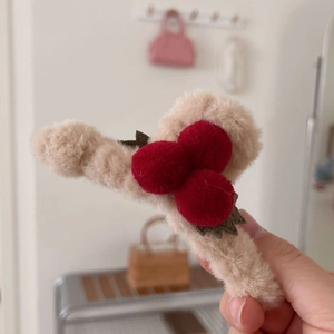 Détail de la pince à cheveux cerise en peluche avec pompons rouges et fausse fourrure