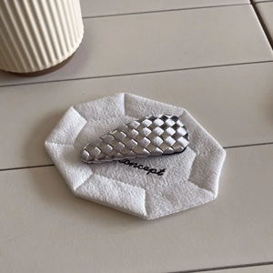 Detail of checkered weave hair clip in silver and black on a textured white surface