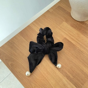 Elegant black velvet bow hair scrunchie with large white pearls on a rustic wood table