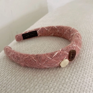 Detail of pink knitted headband with buttons and HAND MADE label on textured background