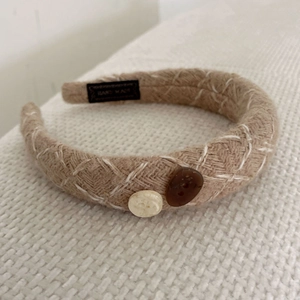 Close-up of beige knitted headband with white cross-stitching and decorative buttons