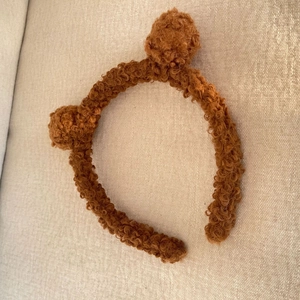 Detailed close-up of brown faux sheepskin teddy bear ear headband on soft fabric