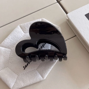 Minimalist black heart-shaped hair claw clip on white fabric with a sleek glossy finish
