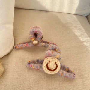Detail of crochet hair clips featuring a smiley face patch and pearl on purple speckled yarn
