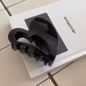 Minimalist black heart-shaped hair claw clip in glossy PC material on a white sketchbook