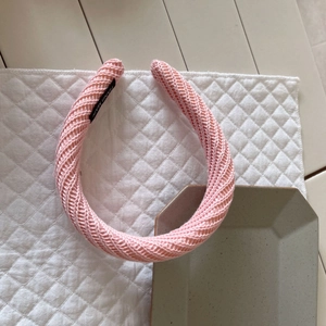 Détail d'un serre-tête rose tricoté avec motif à chevrons et étiquette faite main sur coussin