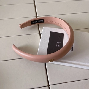 Elegant pale pink leather headband with golden metal letter B ornament on white books