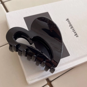 Macro detail of glossy black heart-shaped hair claw clip with interlocking grip teeth