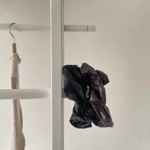 Detailed view of black and coffee vintage textured leather scrunchies set on white shelf