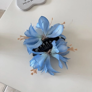 Gros plan de fleurs de lys en tissu bleu sur une pince à cheveux en plastique noir