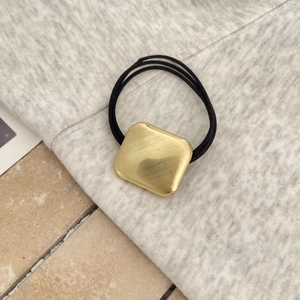 Detail of square golden brushed metal charm on a black high-elasticity braided hair tie
