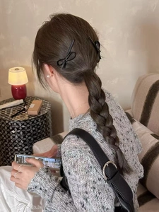 Detail of two minimalist black bow hair clips styled on a woman's dark brown braided ponytail