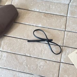 Minimalist black leather bow hair clip with litchi texture on a marble background