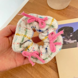 White knitted scrunchie with colorful dots and three pink bows on wooden background