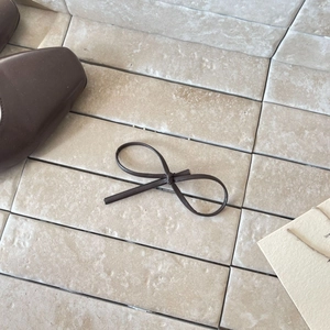 Elegant dark brown leather bow hair clip with fine stitching on a vintage tile background