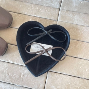 Detail view of black and brown leather bow hair clips on a heart shaped tray