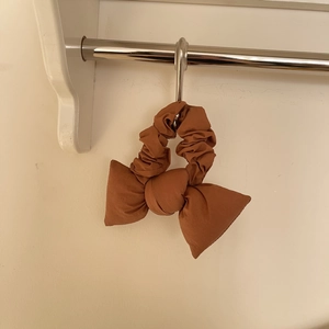 Détail d'un chouchou noeud en coton marron caramel avec texture plissée sur un support