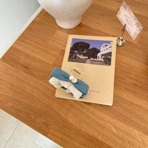 Denim blue bow hair claw clip with pearls and lace on a book over a wooden desk