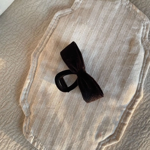 Close-up of black velvet bow hair clip on a beige linen surface for autumn winter