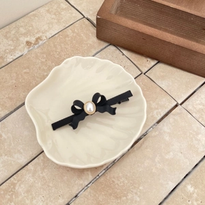 Pince à cheveux élégante avec nœud noir et perle sur un plateau décoratif en céramique