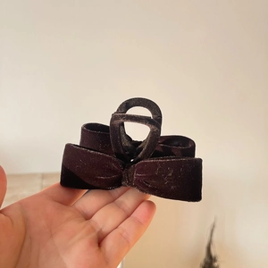 Detailed view of a dark brown velvet bow hair claw clip held by hand against a plain wall