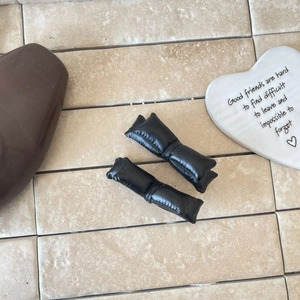 Détail de deux barrettes nœuds en similicuir noir rembourré avec texture plissée