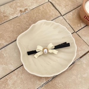 Barrette à cheveux élégante avec nœud et perle en noir et blanc sur plateau décor