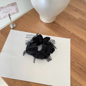 Close-up of a black satin hair scrunchie with sheer organza bows on a minimalist background