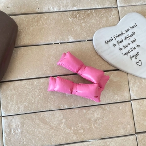 Gros plan détaillé de deux barrettes nœuds 3D en cuir rose sur une surface en pierre