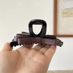 Close-up of a brown leather bow hair claw clip with black glossy base held by hand