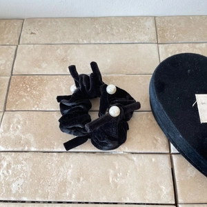 Elegant black velvet bow hair scrunchie with white pearl accents on a beige stone surface