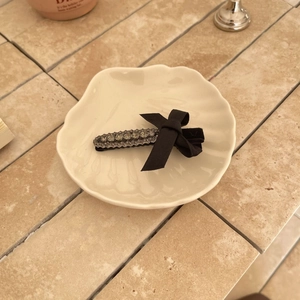 Detail view of a vintage black velvet bow hair clip with sparkling rhinestones on a shell tray
