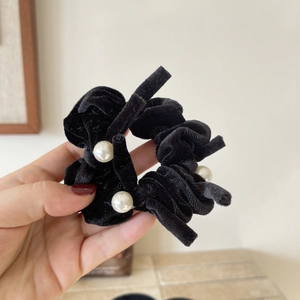 Elegant black velvet hair scrunchie with three white pearls shown in hand on warm background