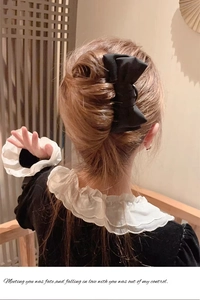 Detail view of a black satin bow hair pin styled in a traditional bun for a refined look
