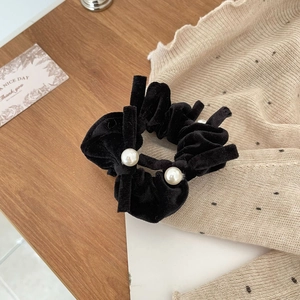 Detail of black velvet scrunchie with white pearls on a soft aesthetic background