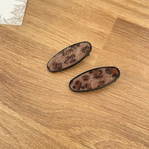 Detail view of two oval leopard print hair clips with faux fur texture on wood background