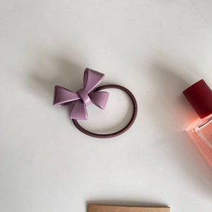 Detail of purple glossy bow hair tie with dark brown elastic band and perfume bottle accessory