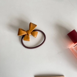 Close-up of mustard yellow resin bow hair tie with dark brown elastic band on white background