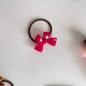 Detailed macro view of an elastic dark coffee hair tie with a shiny magenta resin bow