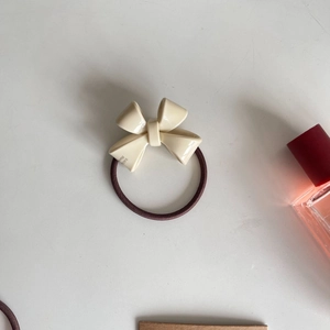 Close-up of cream bow hair tie with shiny resin finish and brown elastic rope detail