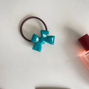 Detailed view of a cyan bow hair tie with a glossy finish and elastic brown rubber band