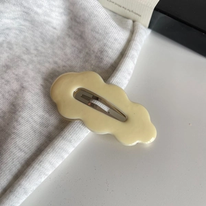 Minimalistische wellenförmige Haarklammer in Creme auf grauem Stoff für einen modernen Look