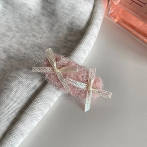 Pink plush hair clip with iridescent bow detail on a grey knit fabric background