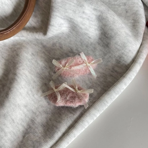 Detail view of plush pink hair clips with white ribbon bows on a knitted background