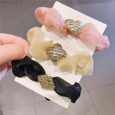 Detailed view of acrylic hair clips with golden alphabet charms on fabric scrunchies