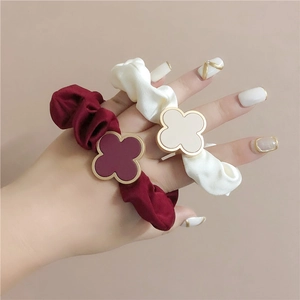 Close-up of silk satin scrunchies in wine red and cream with gold clover charms