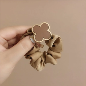 Brown elastic scrunchie with clover charm and glossy fabric for elegant hair styling