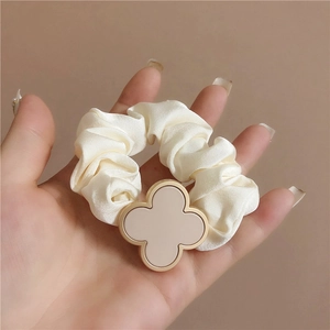 Close-up of elegant cream satin scrunchie featuring a golden four-leaf clover charm