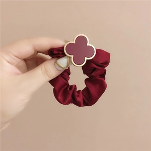 Detailed macro view of a wine red satin scrunchie with a gold-edged clover ornament