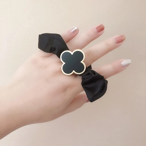 Detail of a black satin scrunchie featuring a luxury gold clover charm on a model's hand